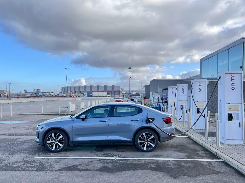 A sleek electric car charging at an Ionity station on a cloudy day in an industrial area.